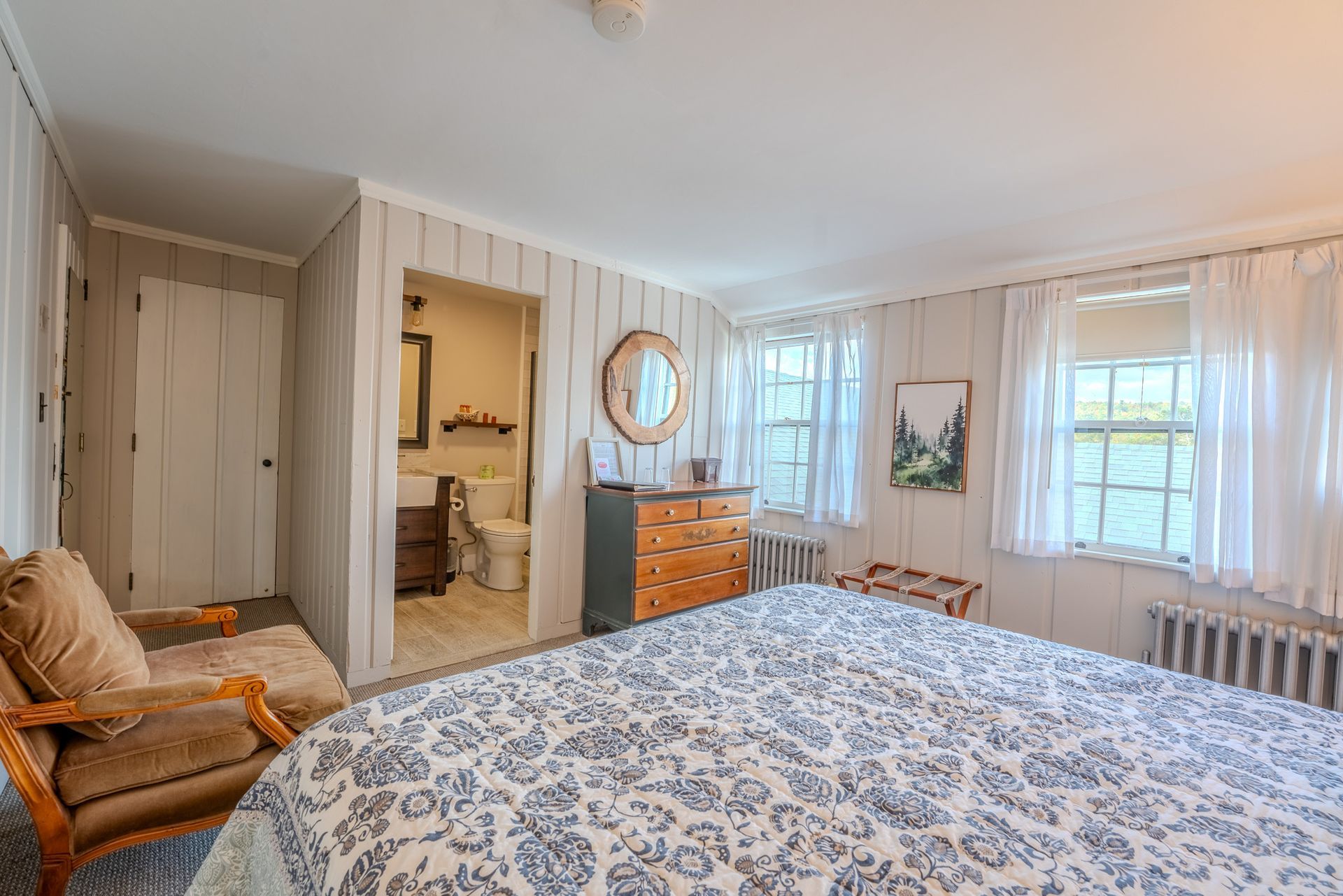 Bedroom with queen bed, armchair, dresser, windows, and bathroom entrance.