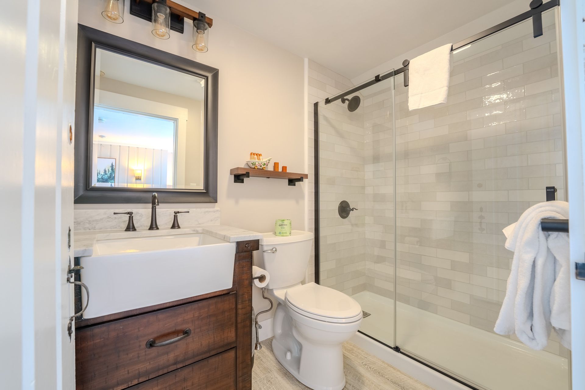 Bathroom with white and gray tiled shower, dark wood vanity and mirror, and a sliding glass door.