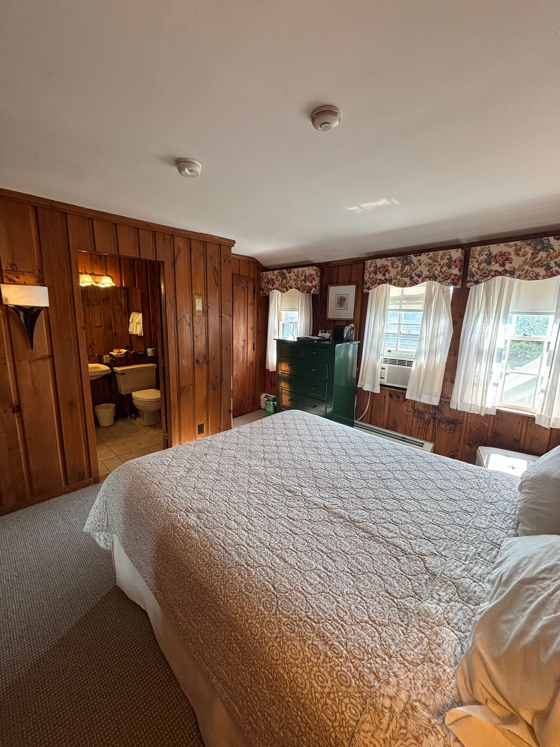 Bedroom with wood-paneled walls, a bed, and a small bathroom visible.