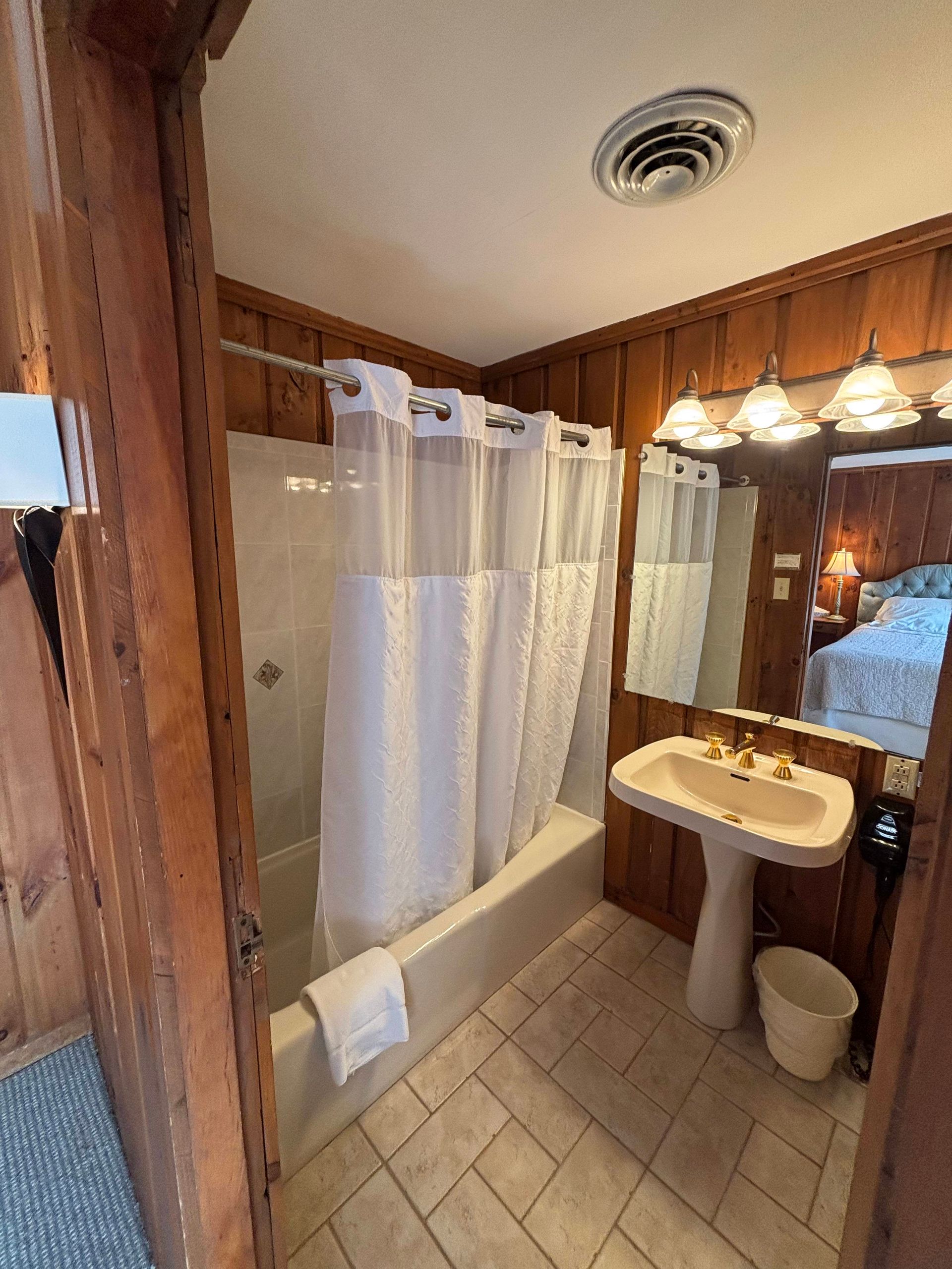 Bathroom with a white bathtub, sink, and shower curtain. Wood paneling on the walls.