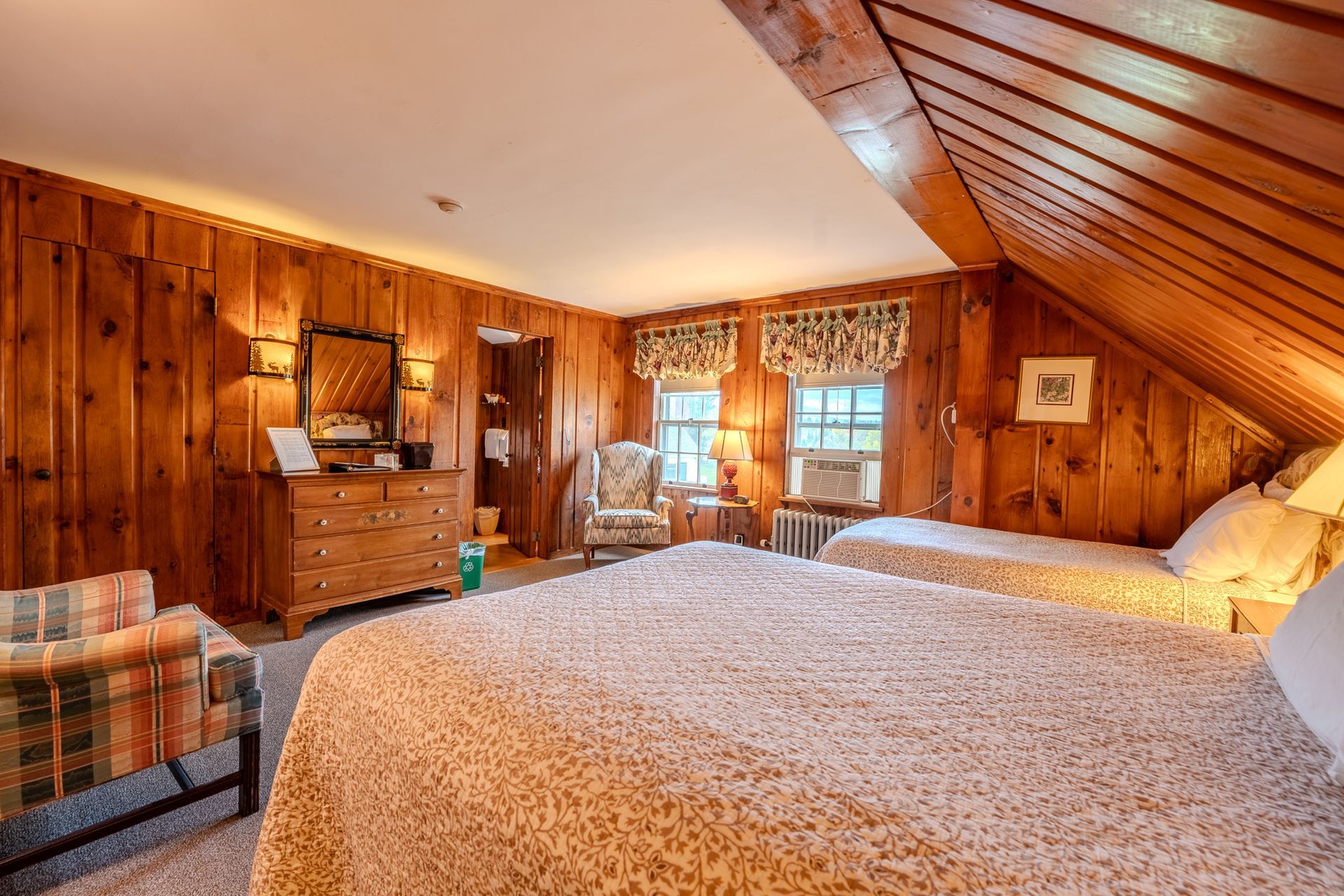 Bedroom with wood-paneled walls, two beds, a dresser, and a patterned armchair.