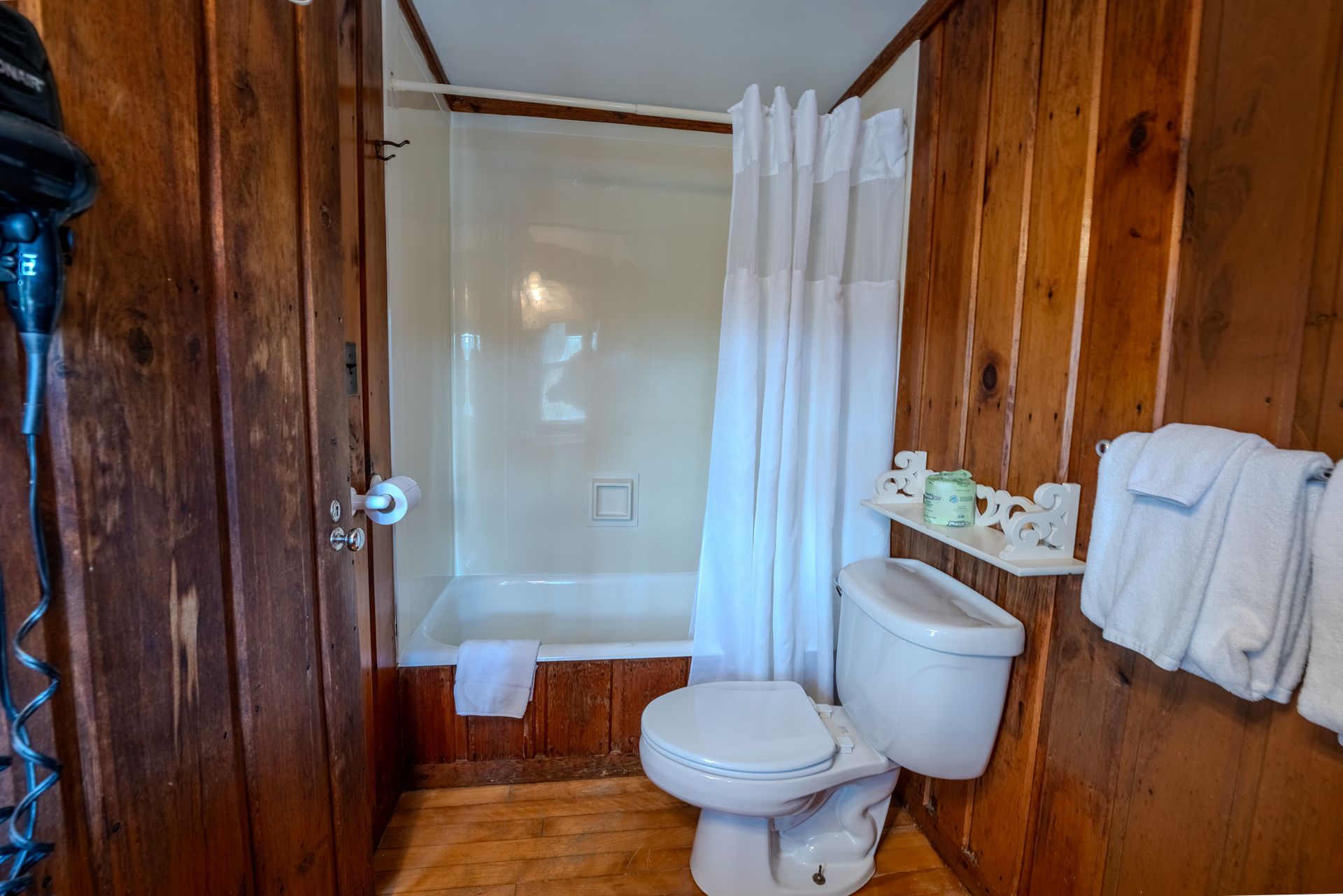 Bathroom with wood-paneled walls, white shower, toilet, and towels.