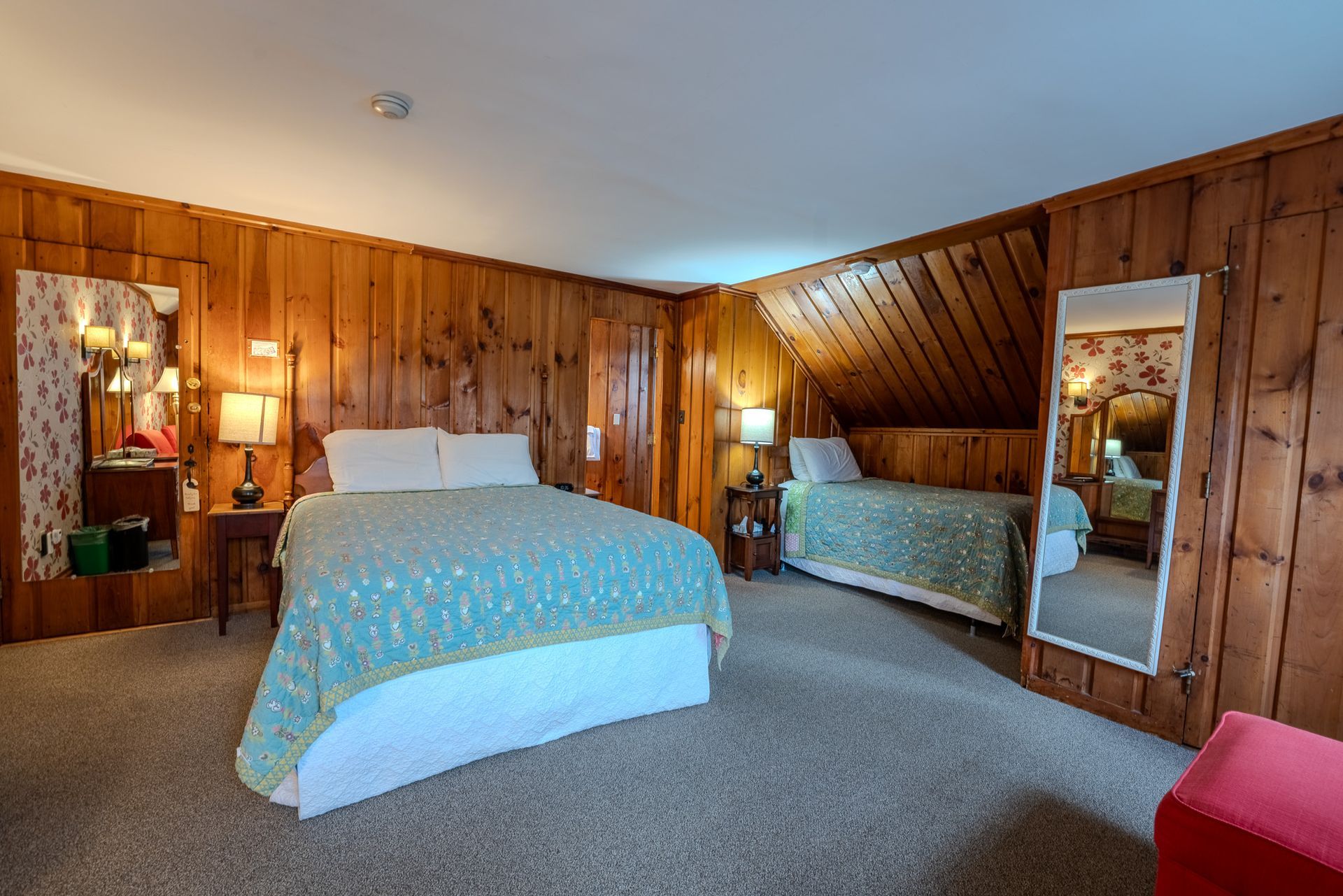 Bedroom with two beds, wooden paneling, and mirrors.