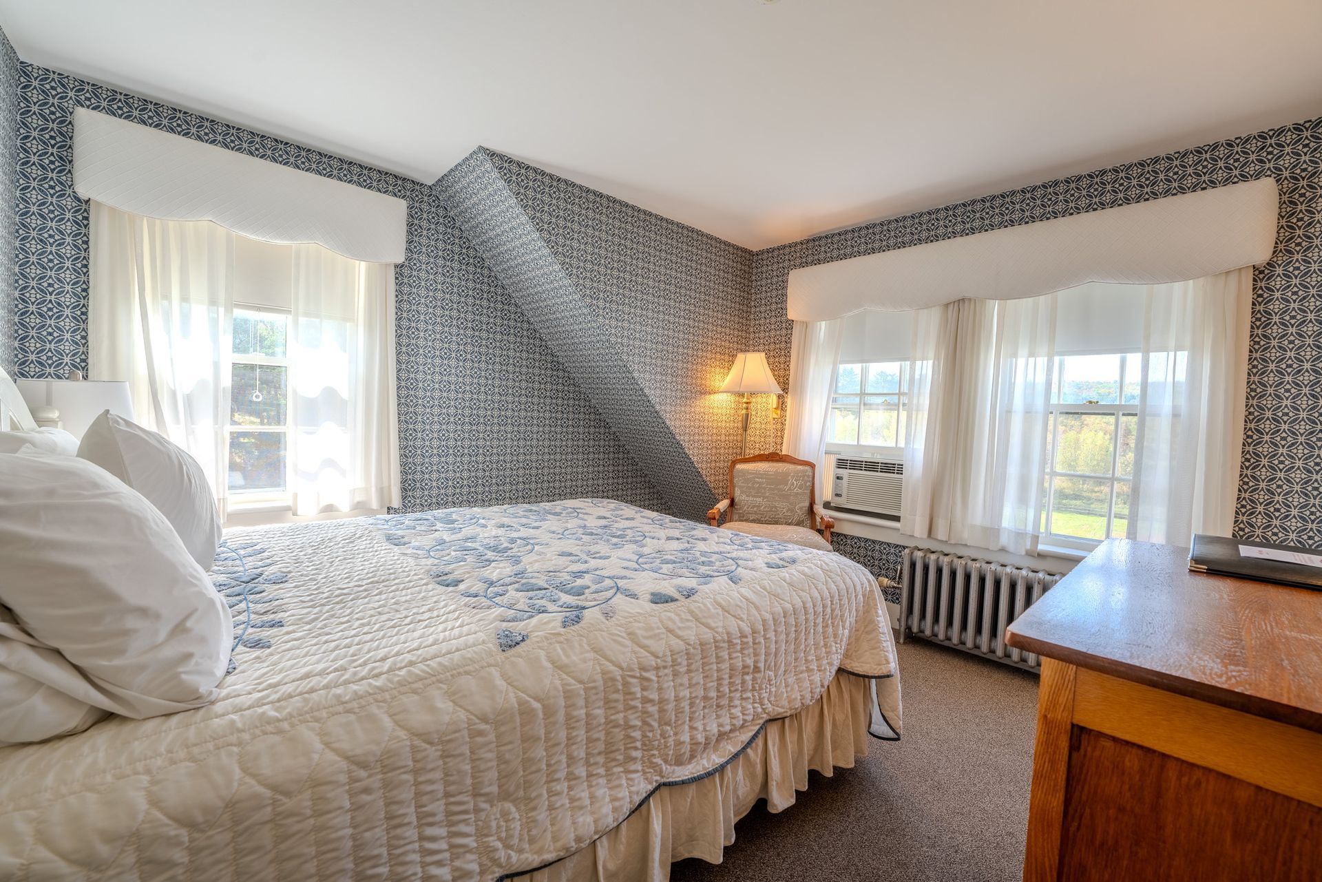 Bedroom with bed, windows, patterned wallpaper, and brown wooden furniture.