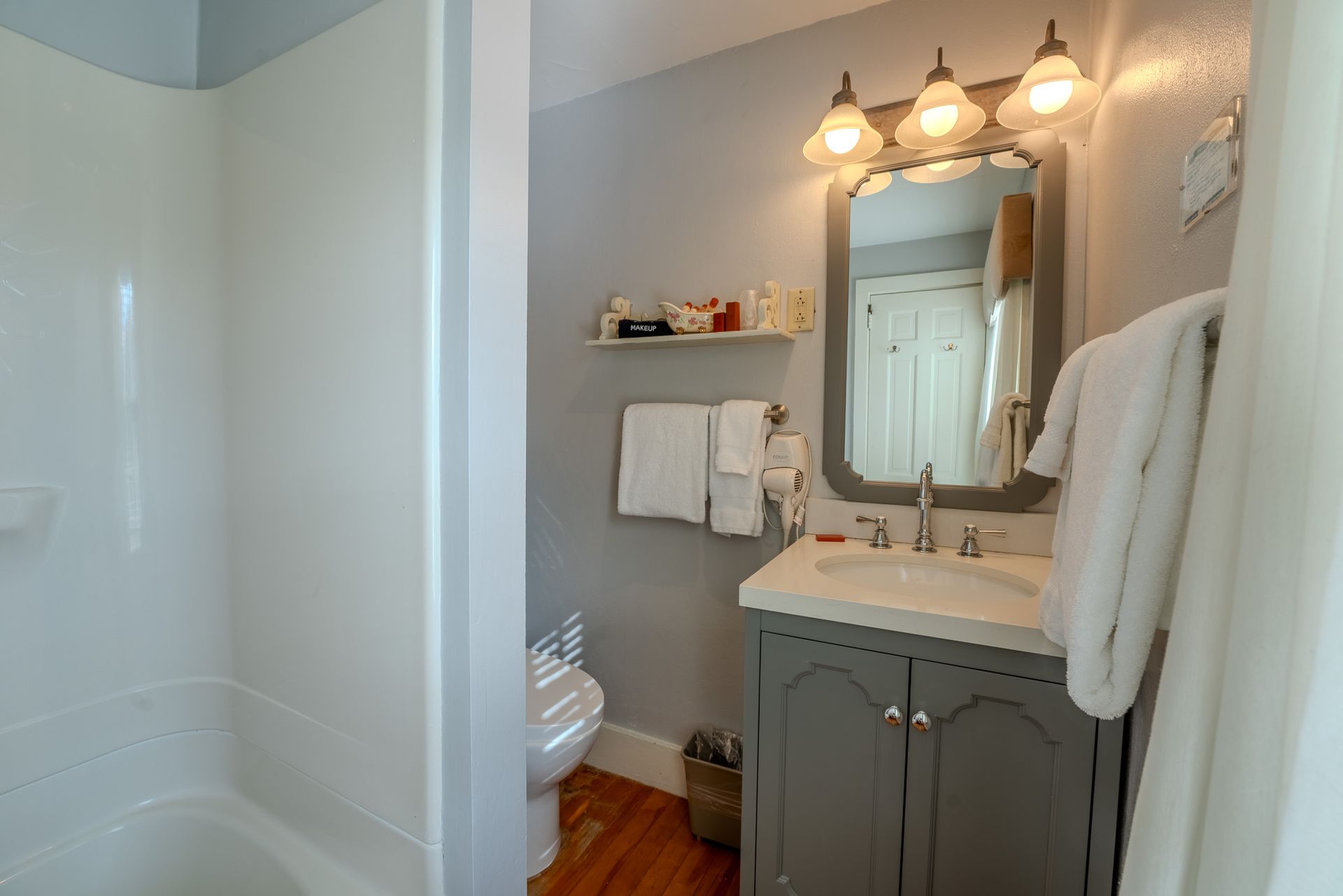 Bathroom with a vanity, mirror, toilet, and bathtub. Gray and white tones, towels hanging.