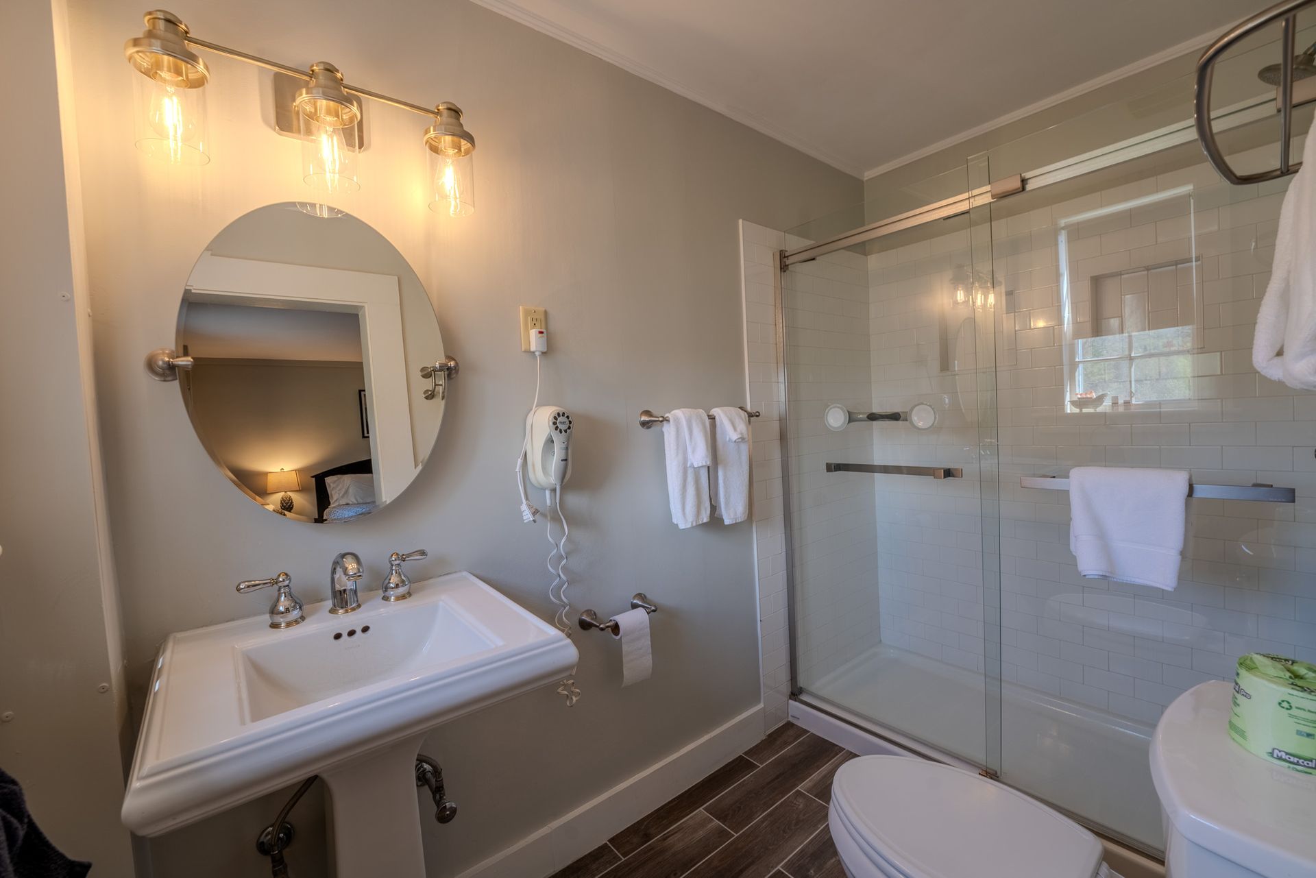 Bathroom with pedestal sink, shower, toilet. Gray walls, bright lights.