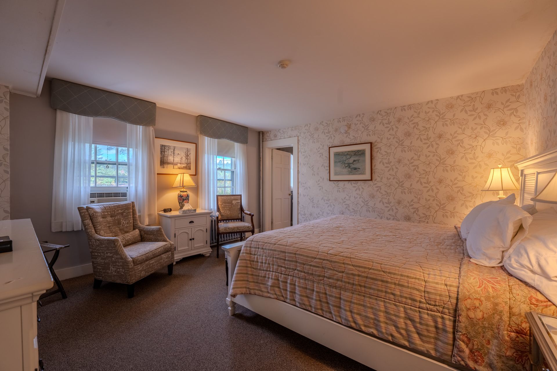 Cozy bedroom with floral wallpaper, double bed, two armchairs, and bedside lamps.
