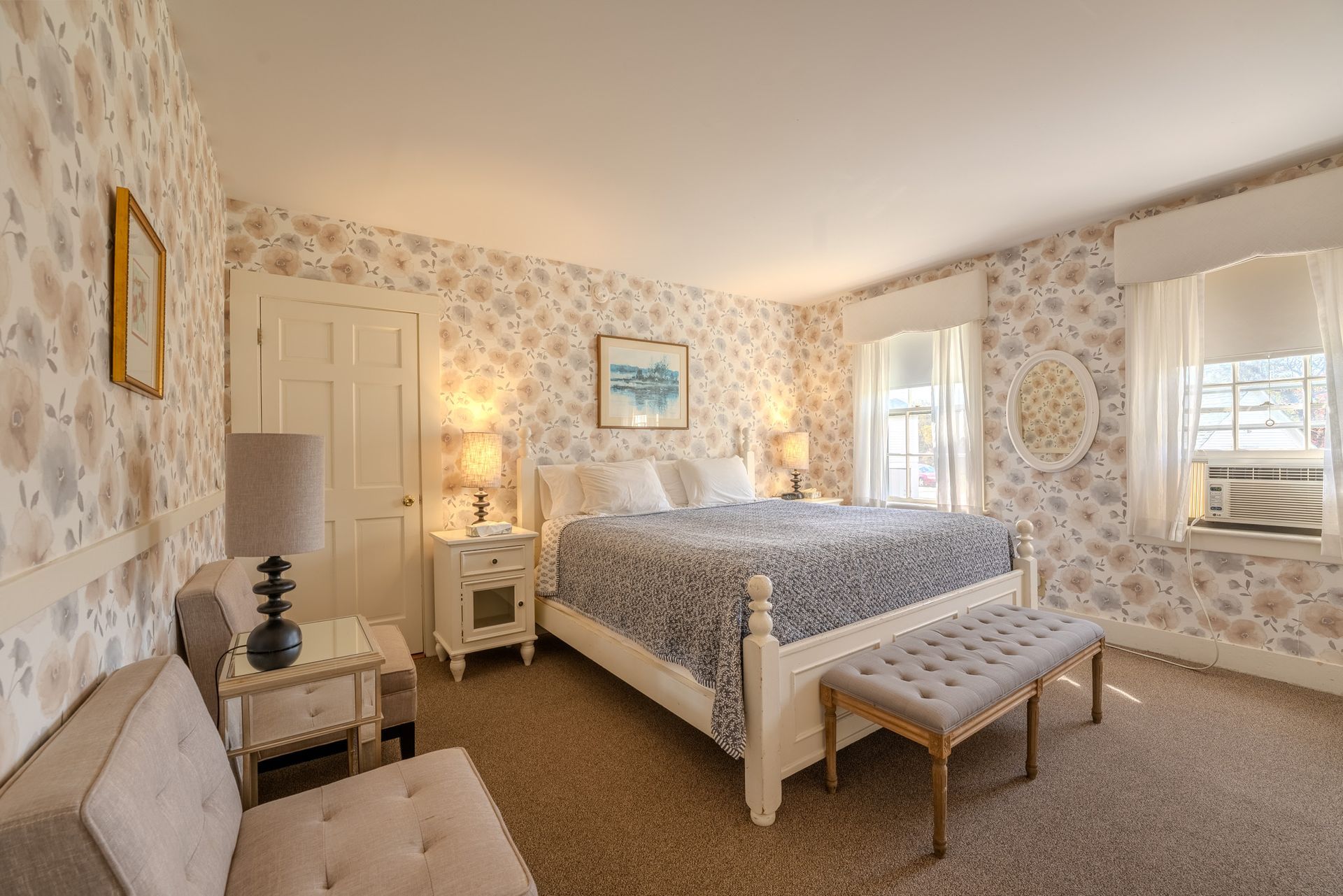 Bedroom with floral wallpaper, king bed, white furniture, window, and seating area.