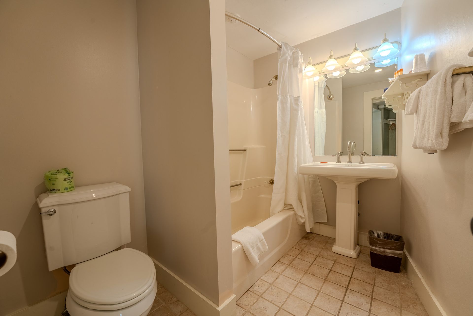Bathroom with toilet, pedestal sink, shower, and beige walls.