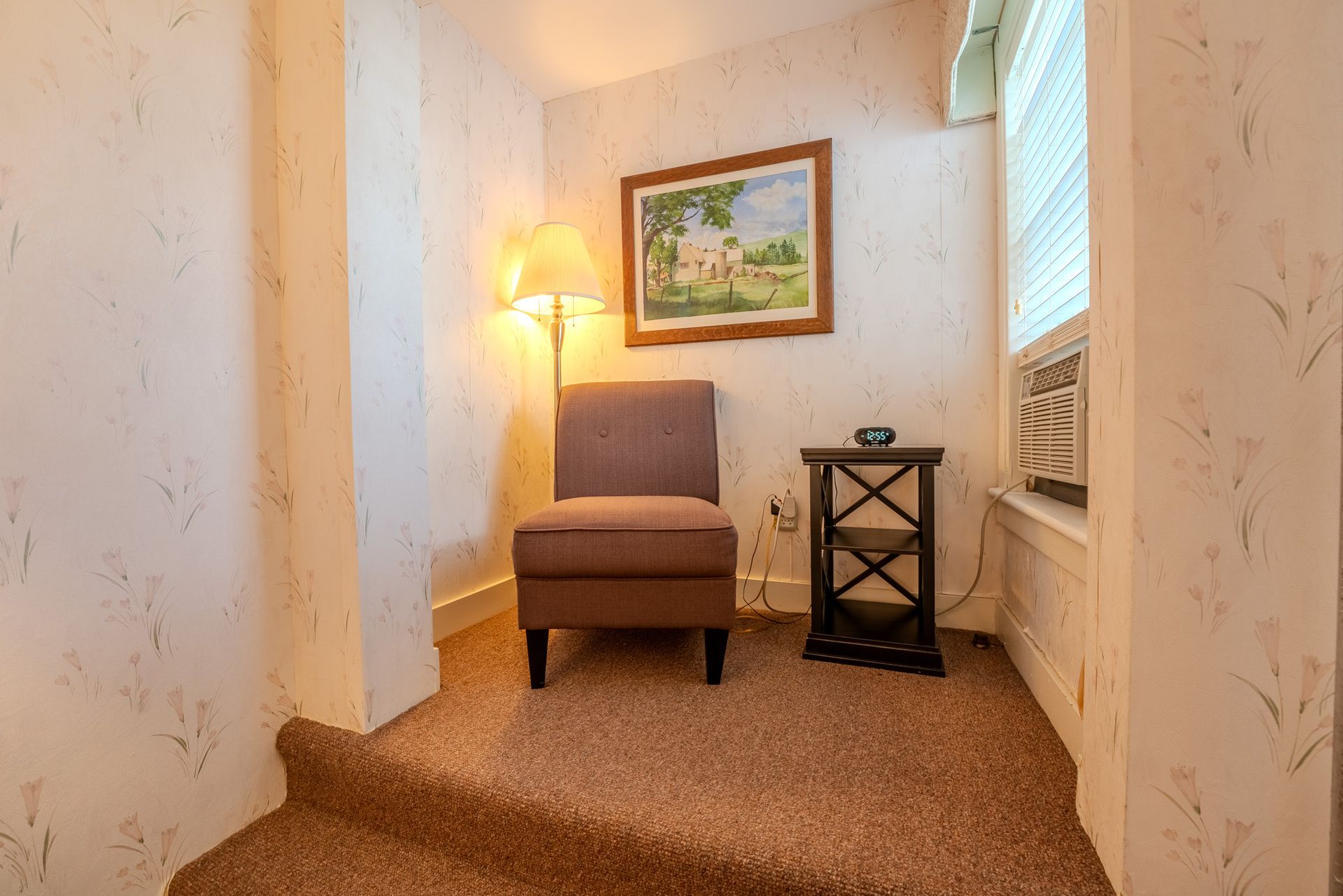 Small reading nook with chair, lamp, painting, side table, and window.