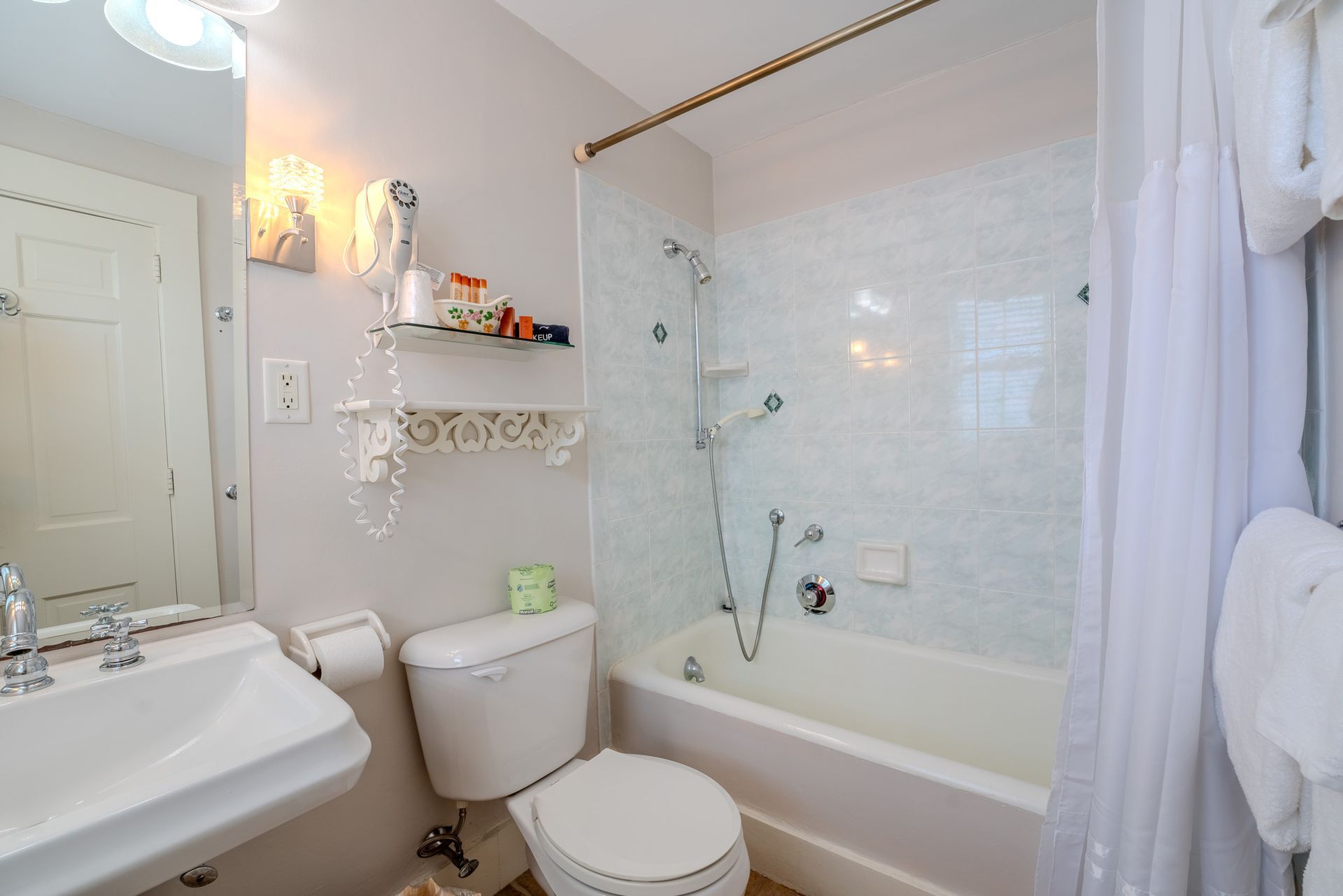 Bathroom with a white sink, toilet, and bathtub. Light walls, glass shower door, and white shower curtain.