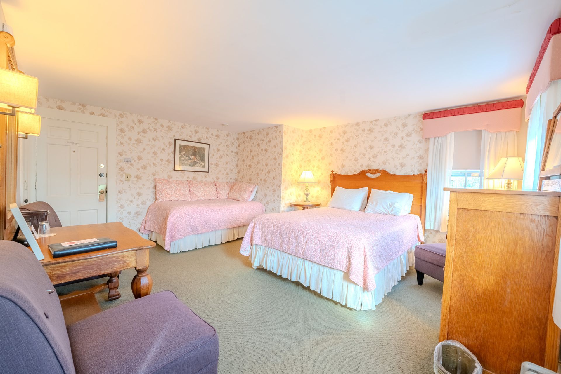 Hotel room with two beds, pink accents, and wooden furniture.