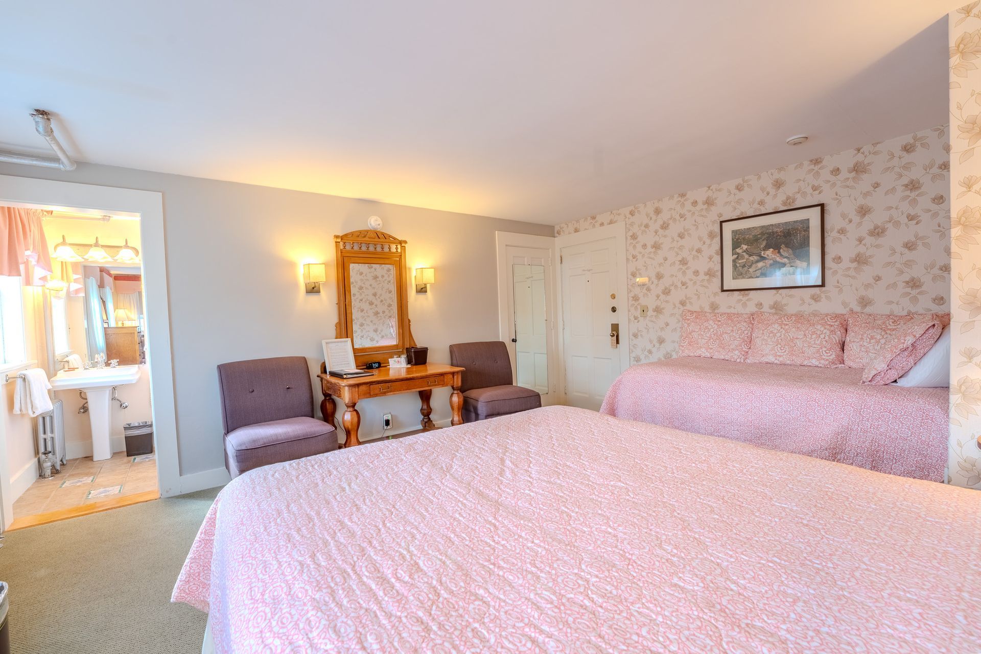 Bedroom with pink bedding, two chairs, vanity, and a daybed.