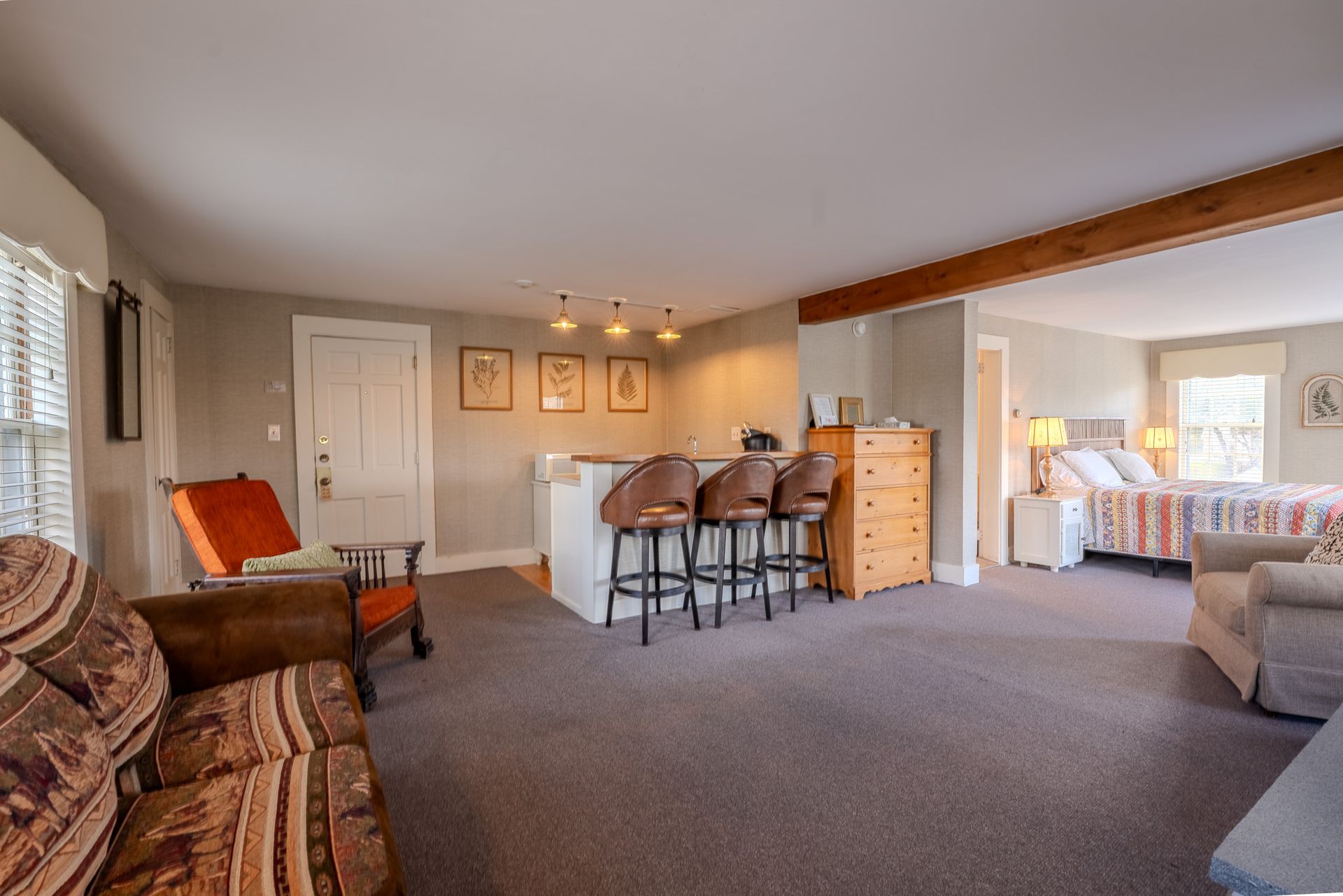 Spacious room with seating areas, bar with stools, a bed, and a dresser.