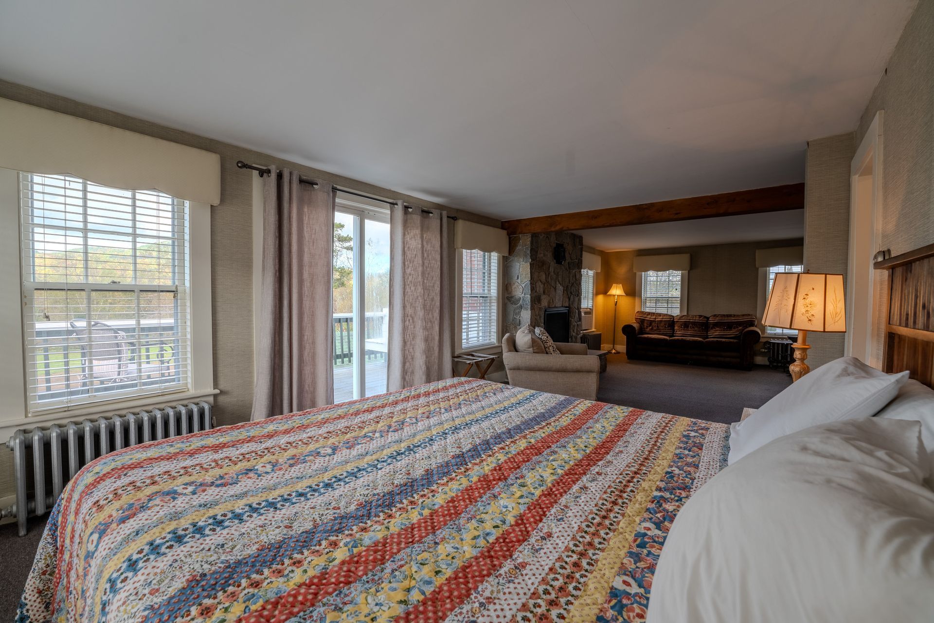 Bedroom with a large bed, windows, a fireplace, and an open doorway to a living room.