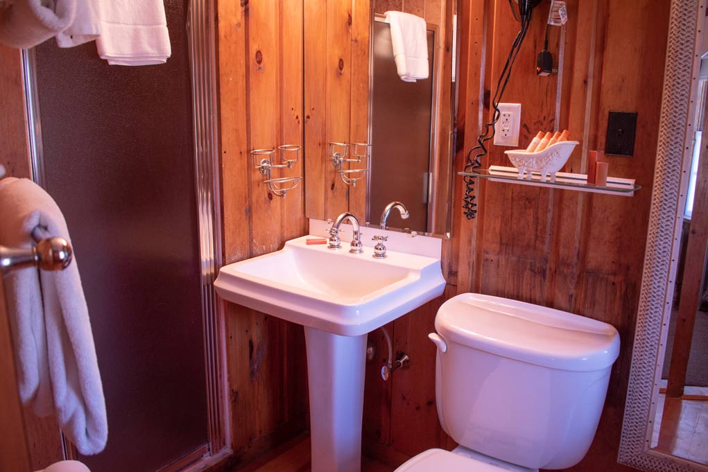 Small bathroom with wooden walls, pedestal sink, and toilet.