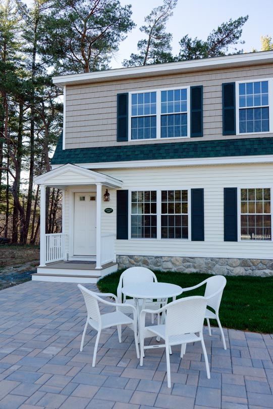 Two-story house with a patio. White table and chairs are on a brick patio.