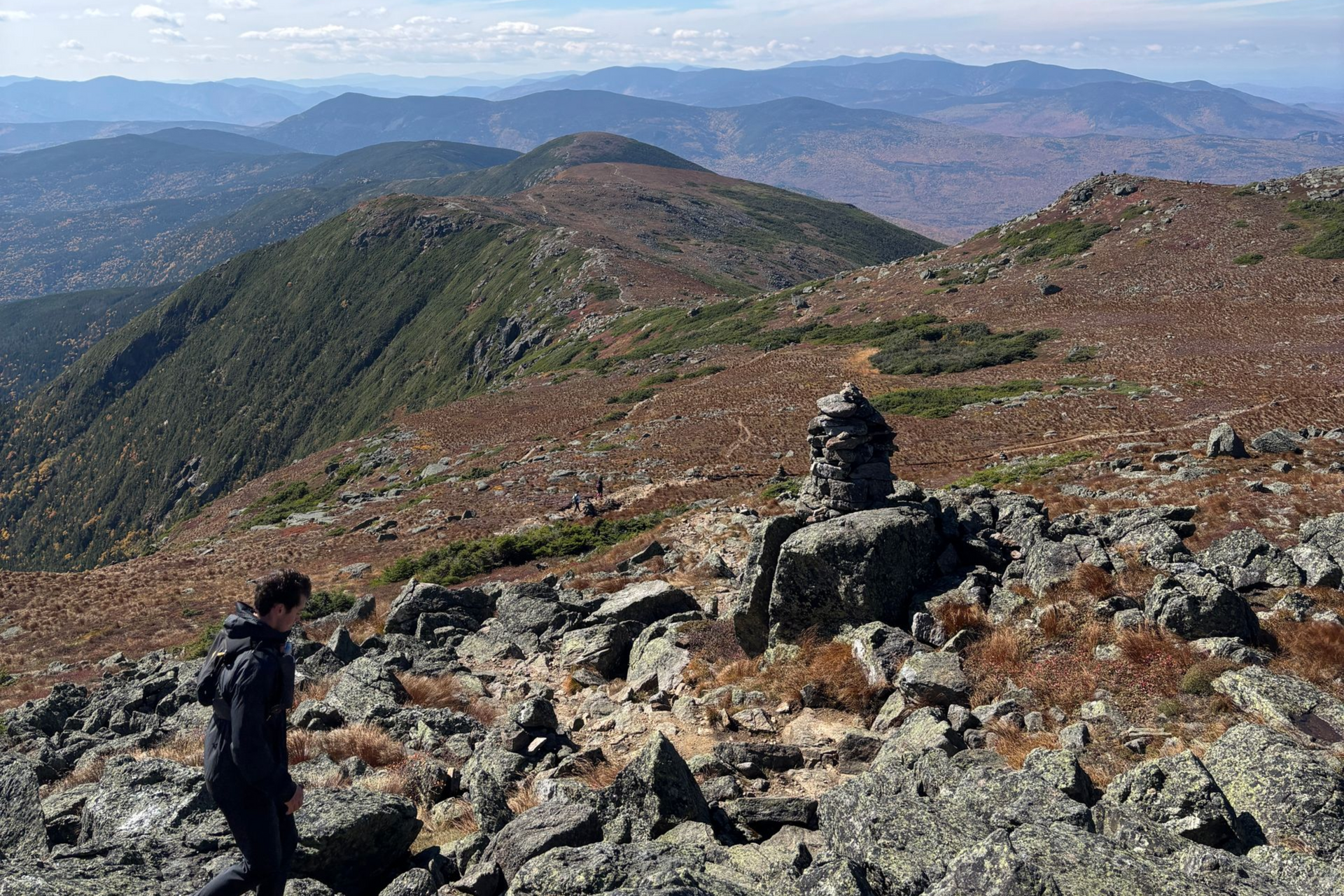 hiker on a rocky ridge trail with mountains in the background