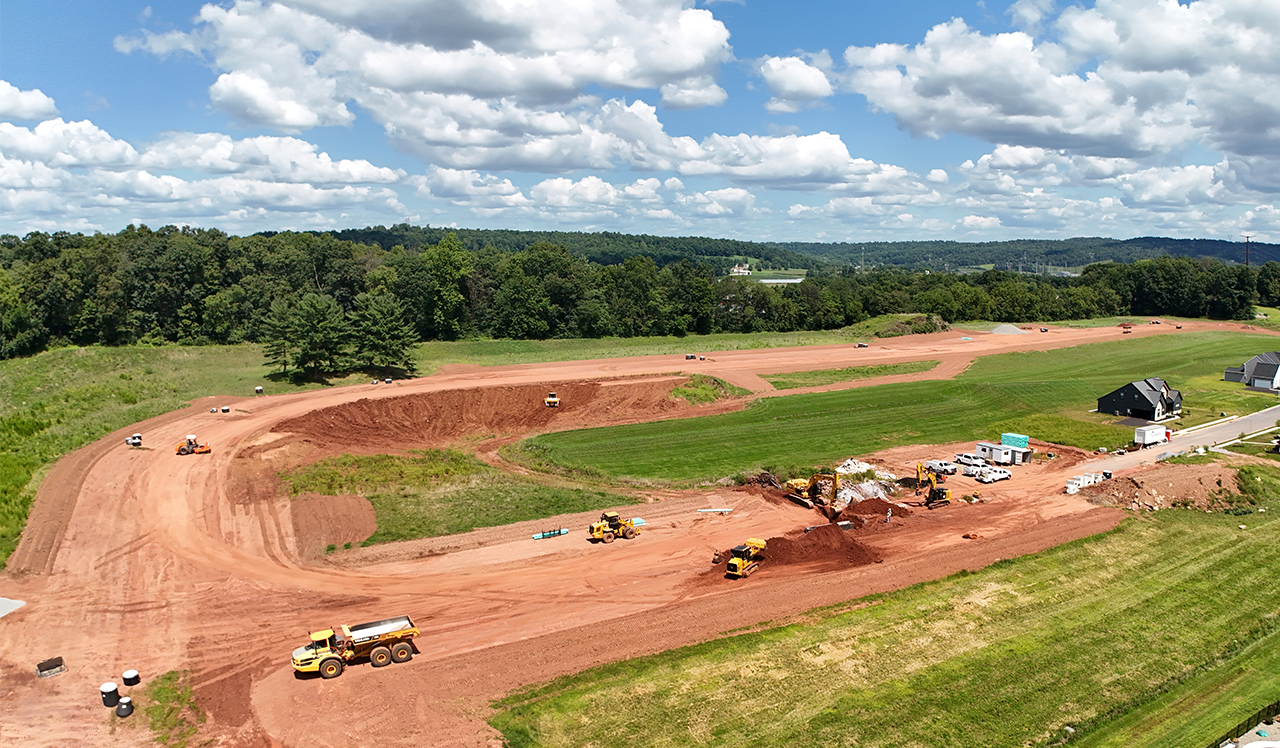 An aerial view of a construction site with a lot of dirt and trees in the background.