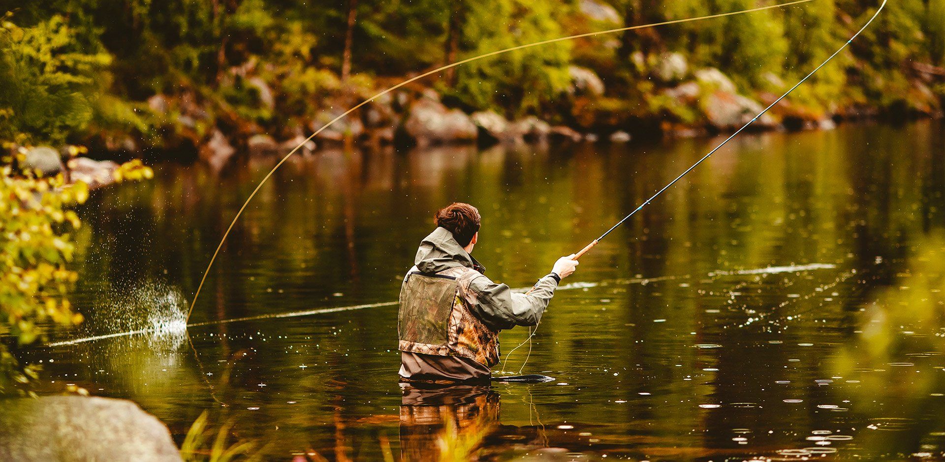 A man is fishing in a river with a fishing rod.