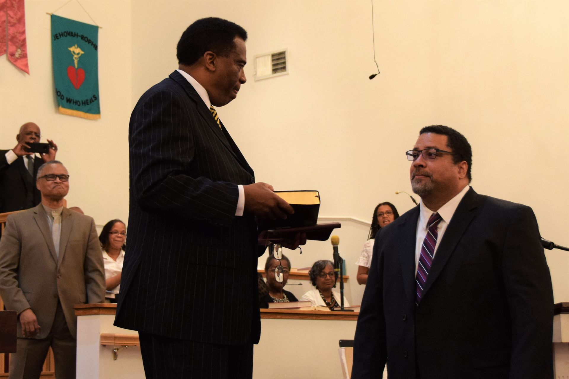 A man in a suit is giving another man a bible