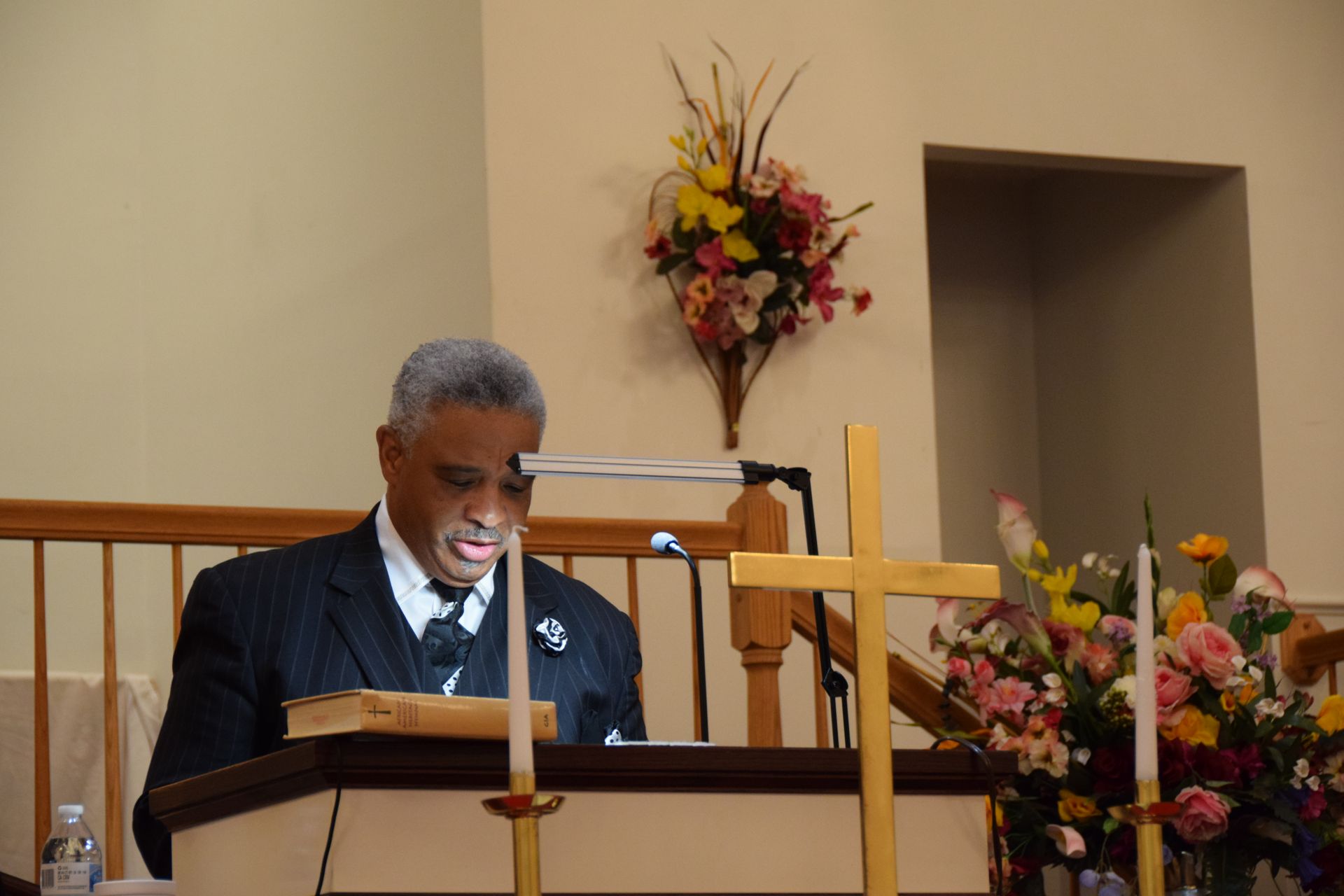 A man in a suit and tie is standing at a podium reading a bible.