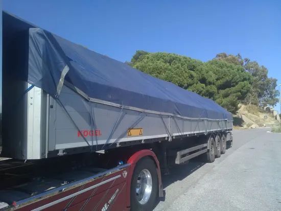 Semirimorchio coperto parcheggiato sul ciglio della strada sotto un cielo azzurro e limpido.