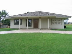 SWain Funeral Chapel building with a tan facade, brown roof, and green lawn. A driveway leads to the entrance.