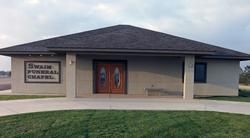 Exterior of Swain Funeral Chapel, beige building with brown double doors, dark roof.