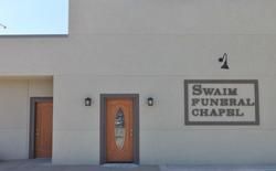 Exterior of Swaim Funeral Chapel with two brown doors, and a sign on a beige wall.
