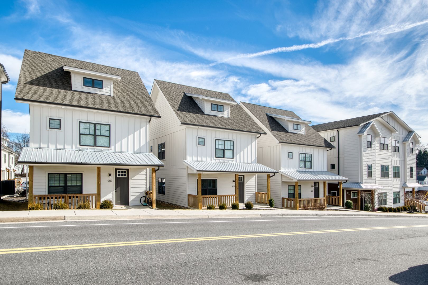 Row of white townhouses with gray roofs and small porches under a blue sky.