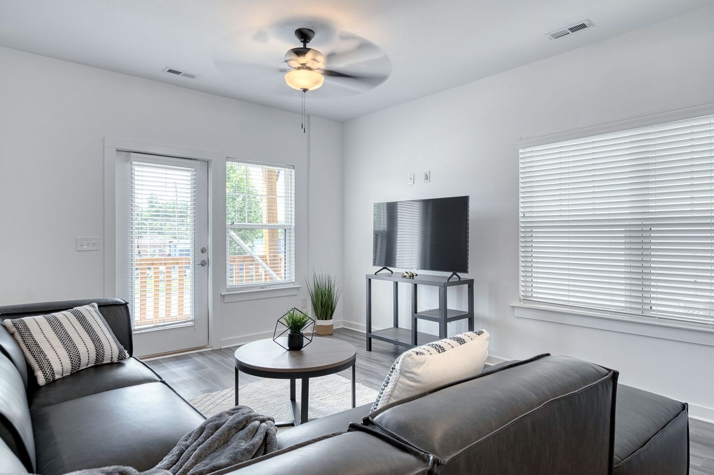 Living room with gray sectional, TV, round coffee table, and door to a deck.