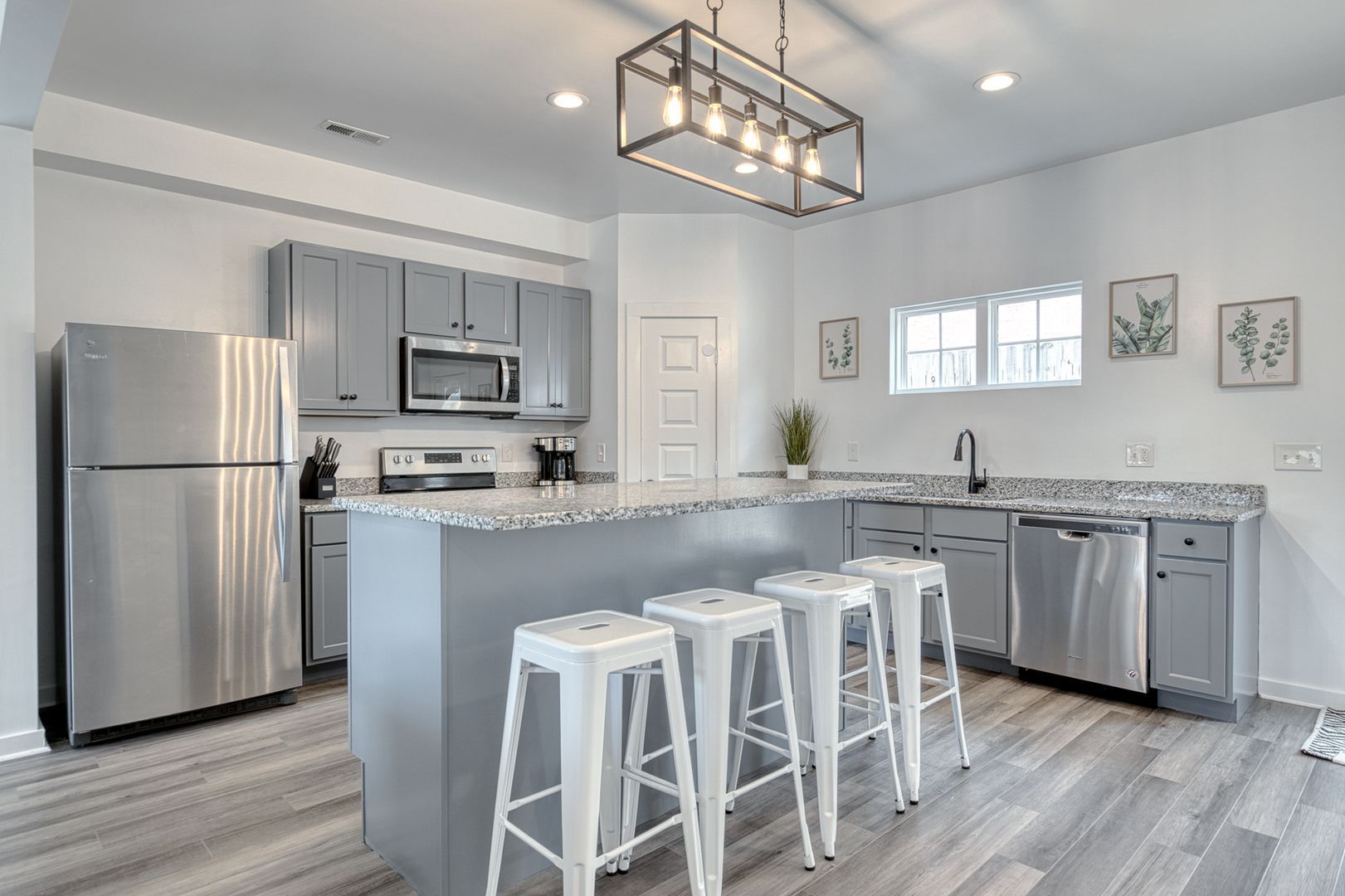 Modern kitchen with gray cabinets, stainless steel appliances, island with bar stools, and light fixture.