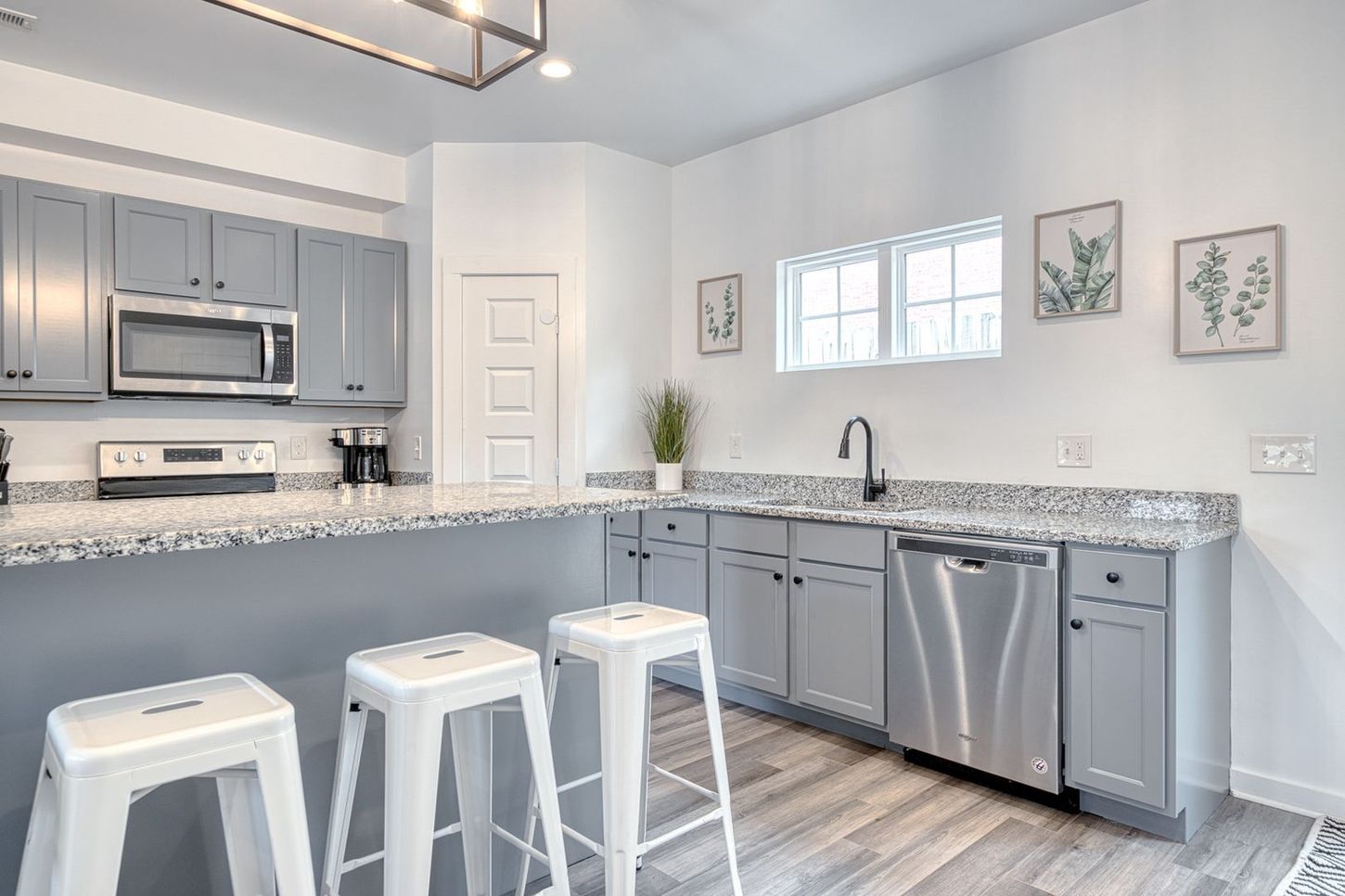 Gray kitchen with stainless steel appliances, white stools, and granite countertops.