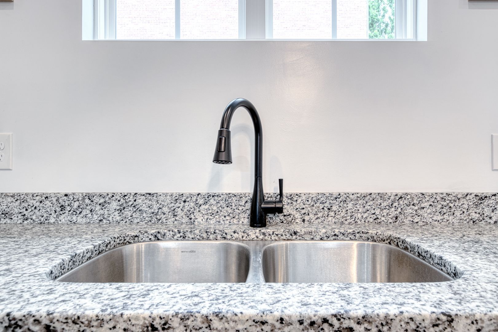 Black faucet over stainless steel double sink on granite countertop in kitchen.