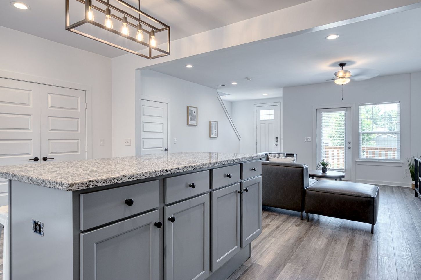Gray kitchen island with granite countertop in a modern, white-walled living space.
