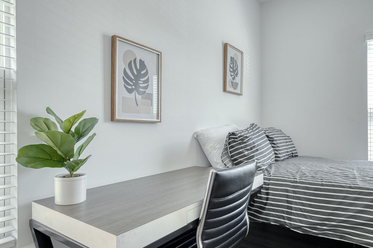 Bedroom with a desk, bed with striped linens, framed art, and a potted plant.