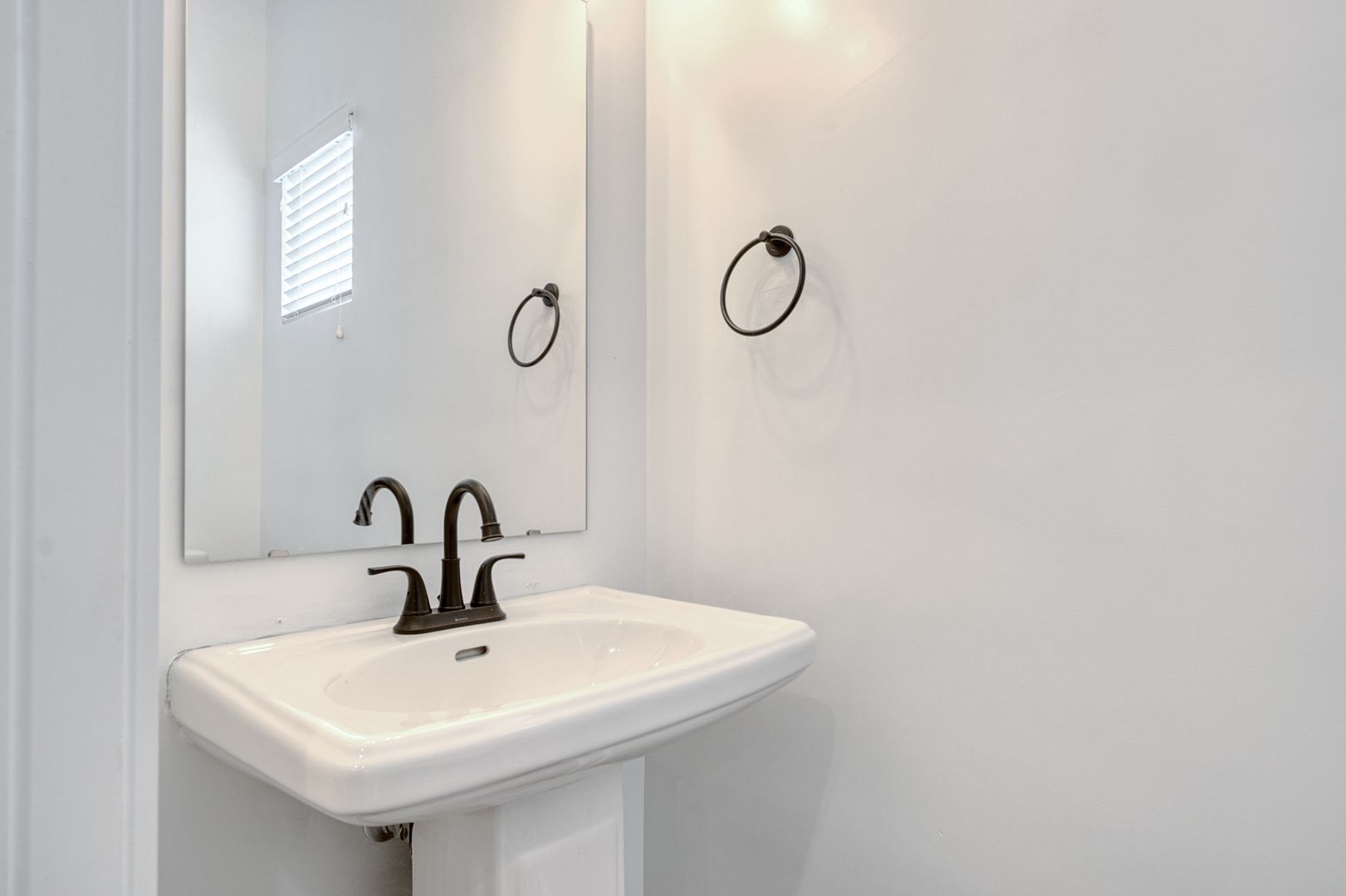 White pedestal sink in a small bathroom; a dark faucet and towel ring contrast the bright walls.