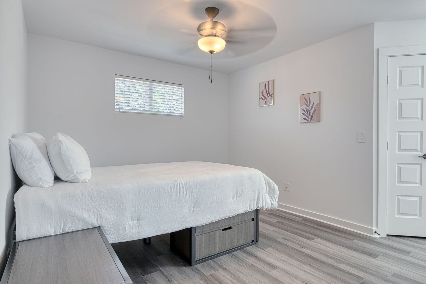 A bedroom with a bed, a small window, and two floral wall art pieces.
