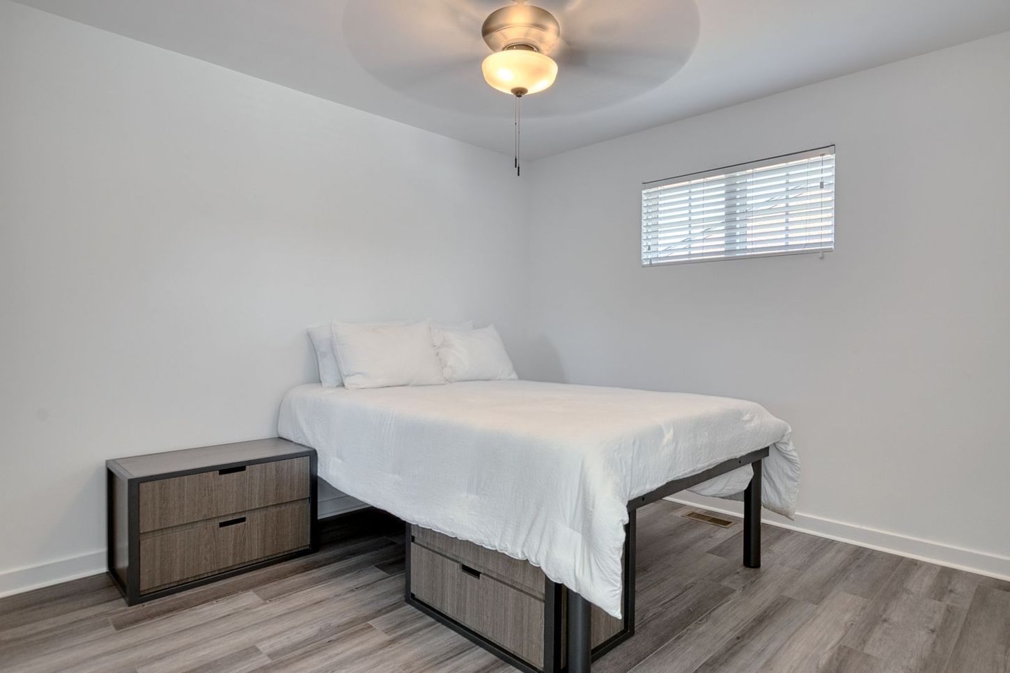 Bedroom with white bedding, a nightstand, and a window with blinds.