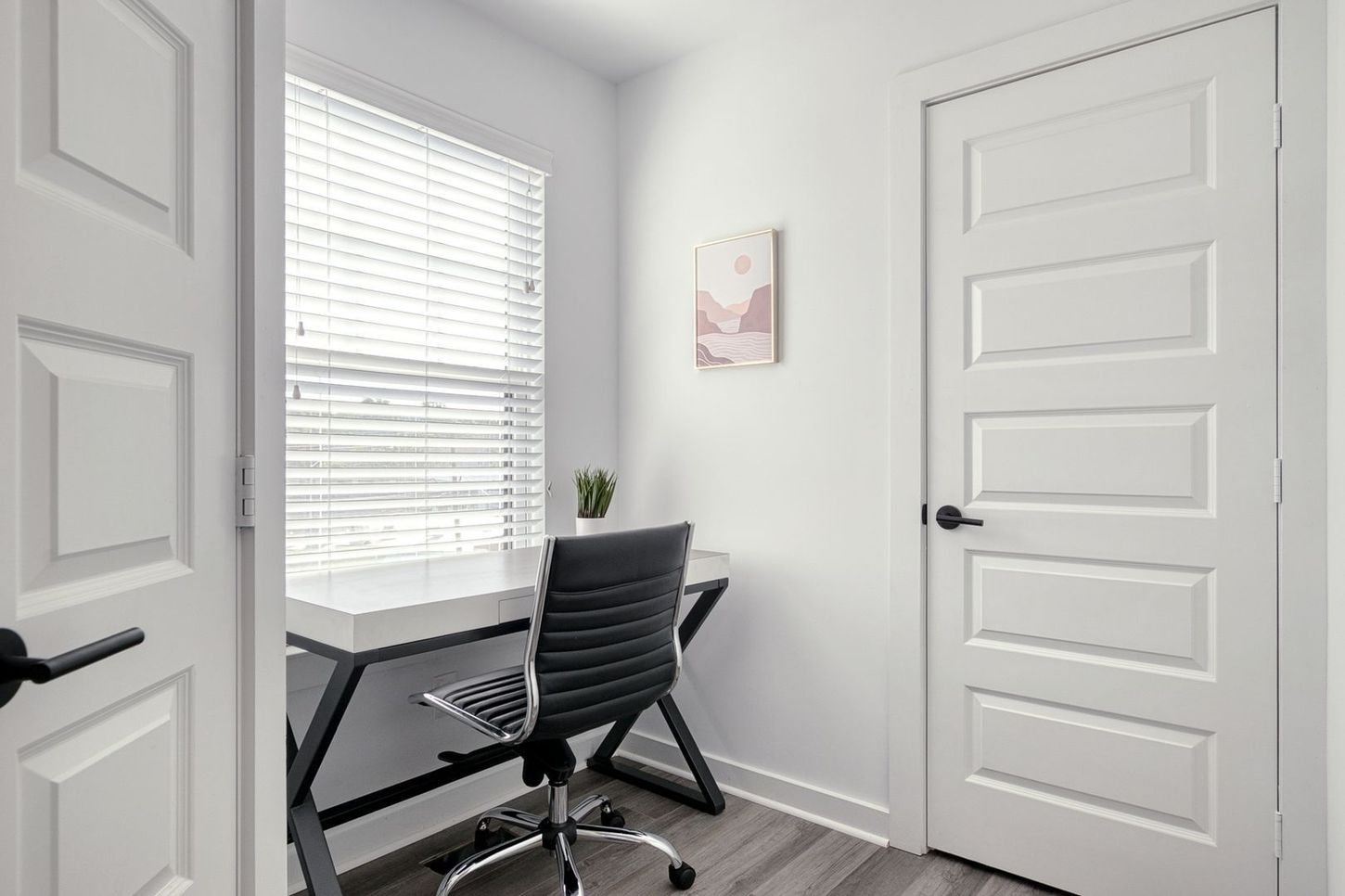 Small white office with desk, chair, and window. A painting hangs on the wall.