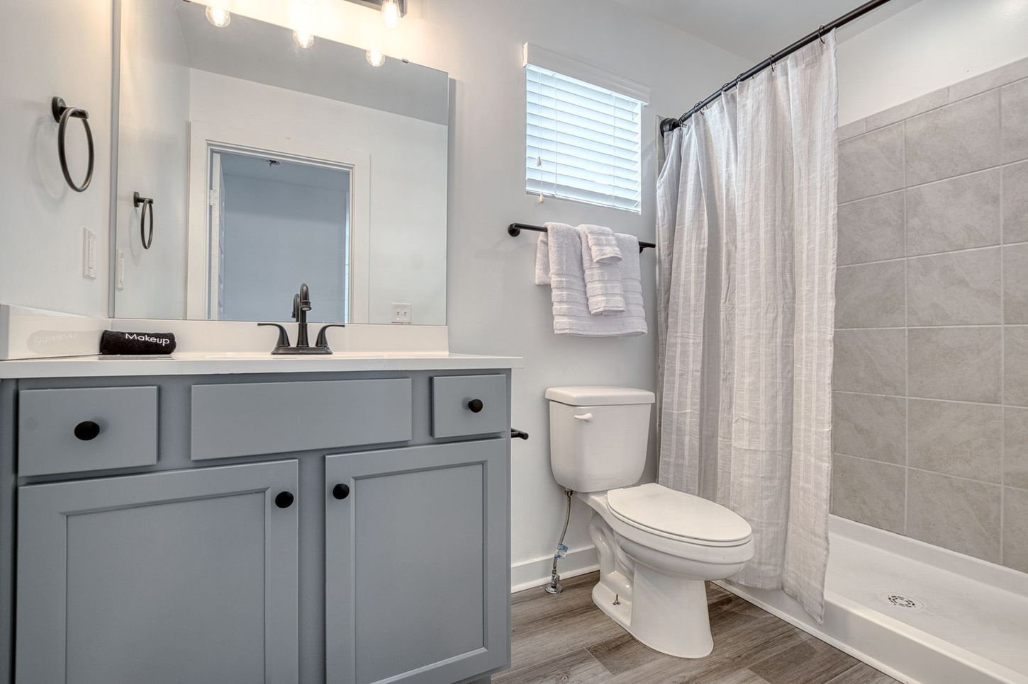 A light blue bathroom with a vanity, toilet, shower, and window.