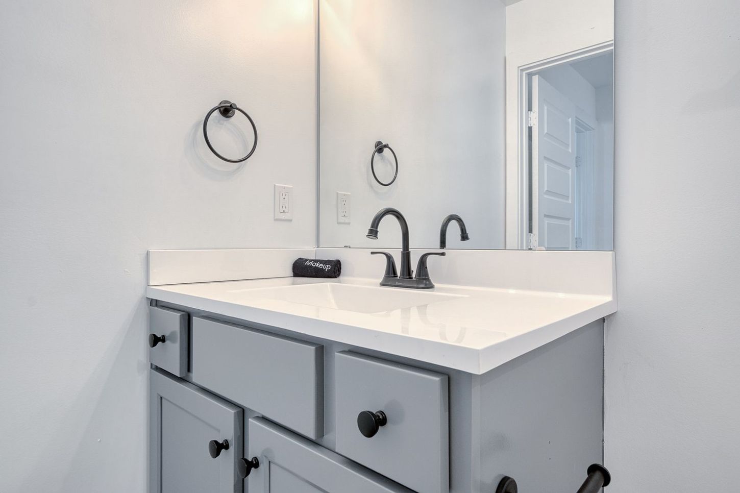 Gray bathroom vanity with white countertop, black fixtures, and round towel ring.