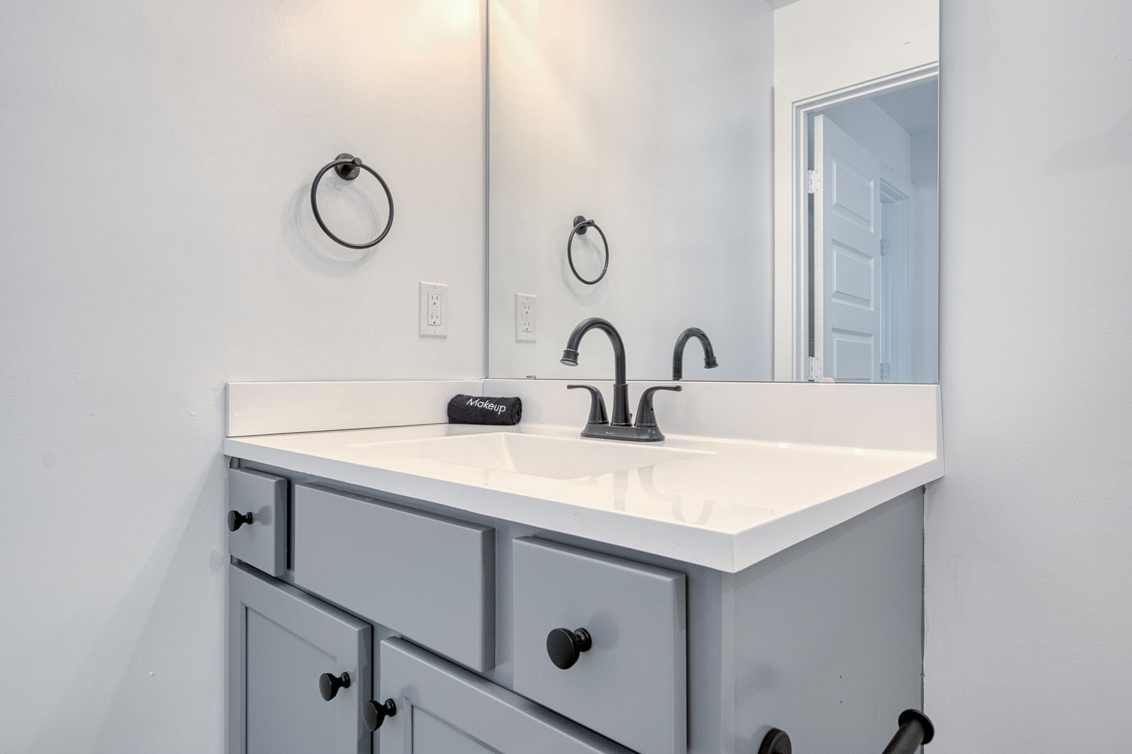 Gray bathroom vanity with white countertop, black fixtures, and round towel ring.