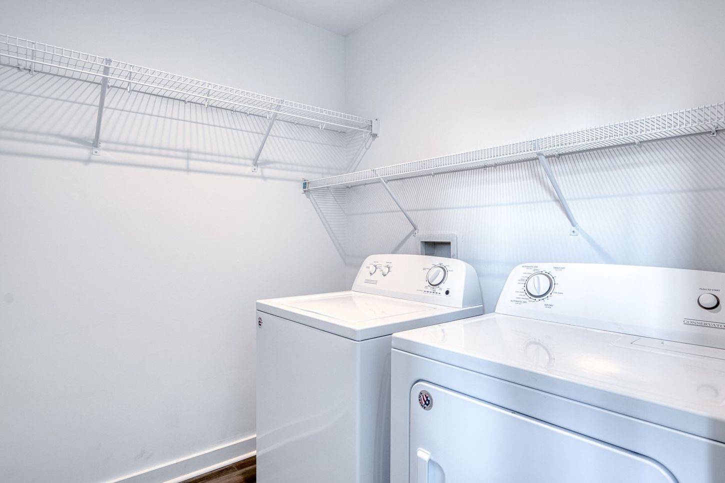White washer and dryer in a laundry room with wire shelving.
