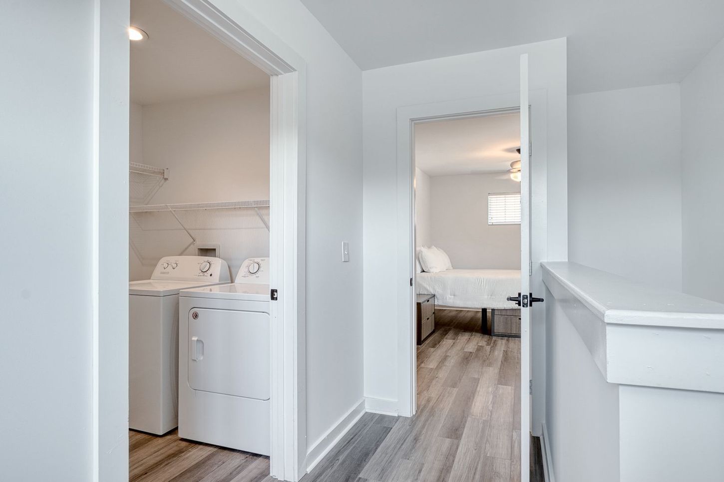 White hallway with laundry room on left and bedroom visible at the end, with wood-look floors.