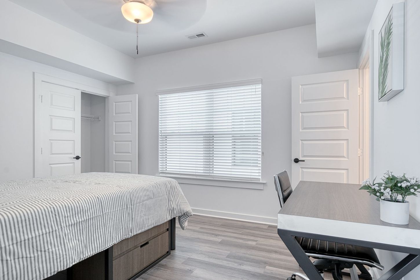 Bedroom with bed, desk, closet, window with blinds, and a ceiling fan.