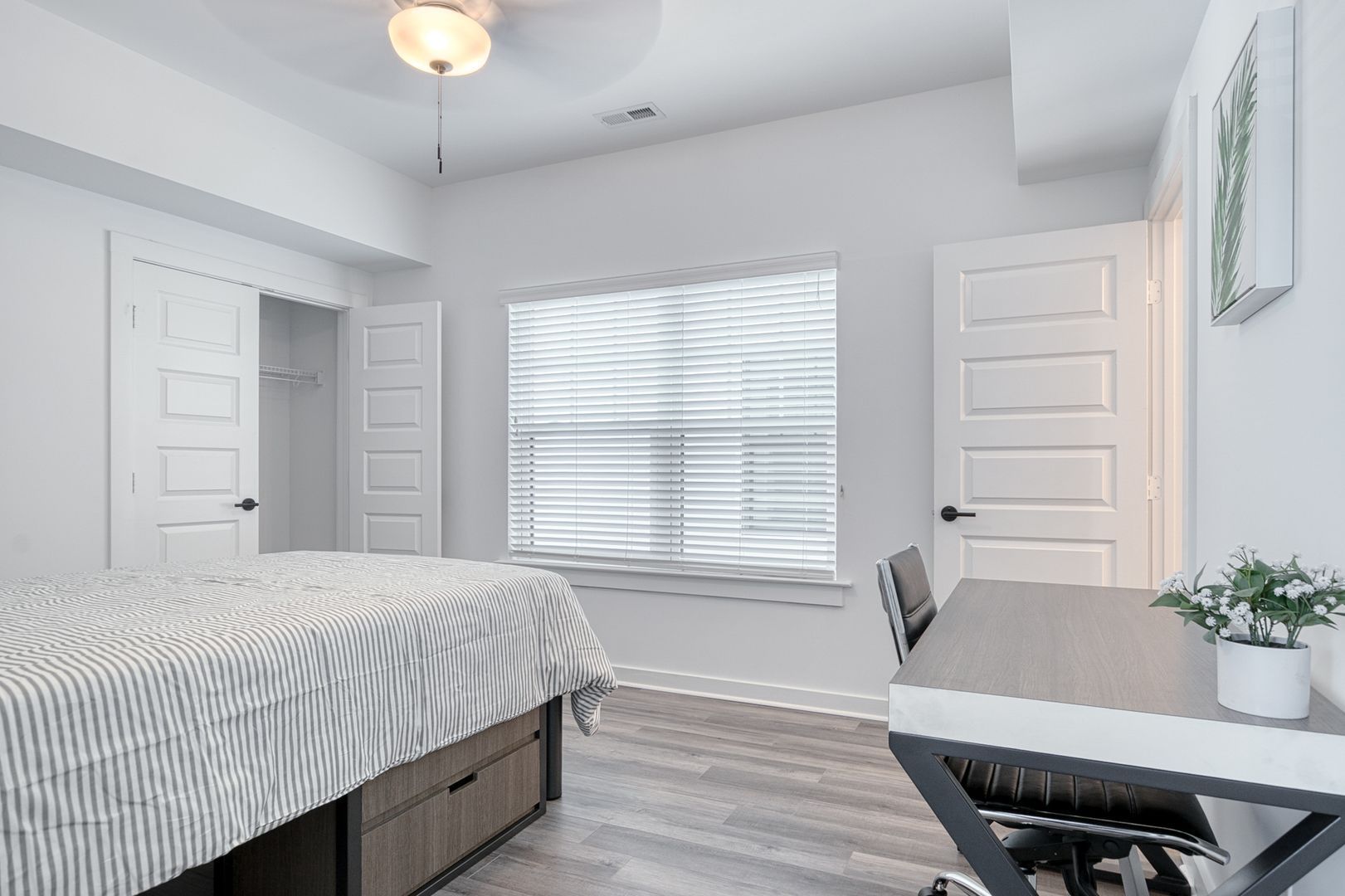 Bedroom with bed, desk, closet, window with blinds, and a ceiling fan.