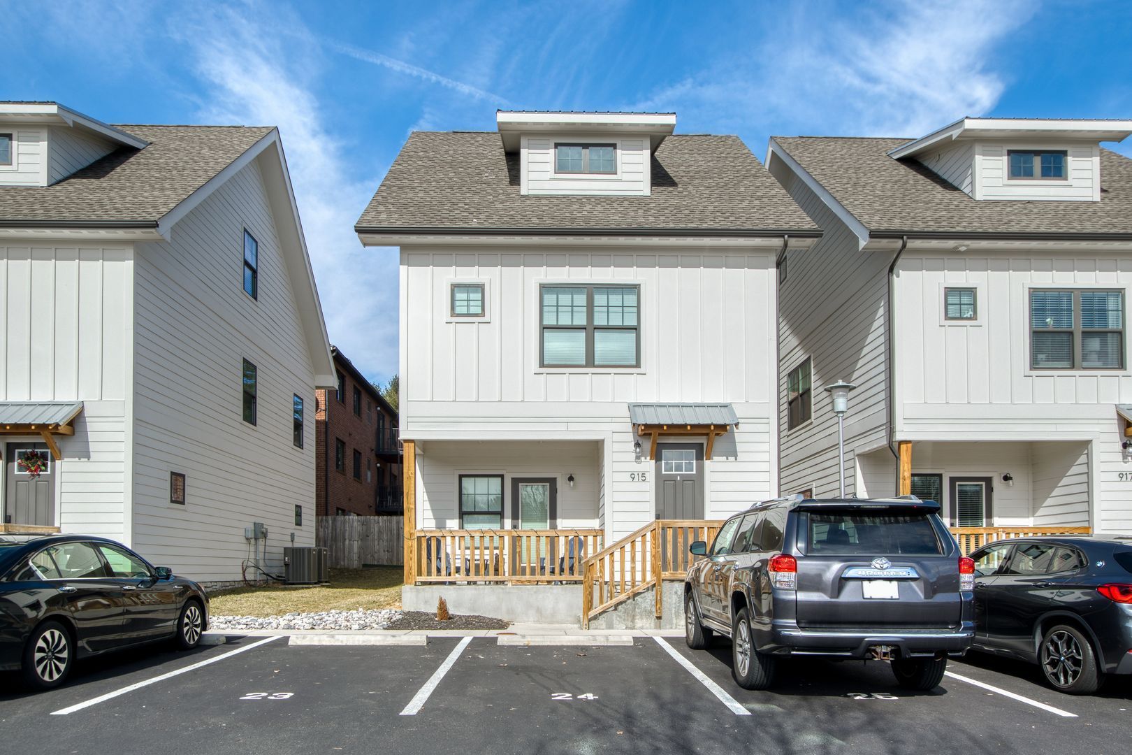 Row of modern white townhomes with parked cars in front, under a blue sky.