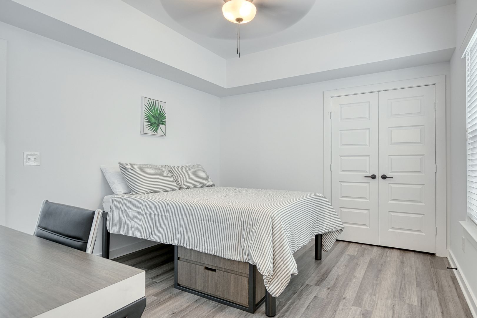 Bedroom with a bed, desk, closed doors, and a window with blinds.